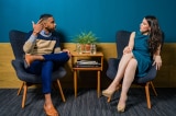 woman wearing teal dress sitting on chair talking to man 2422280